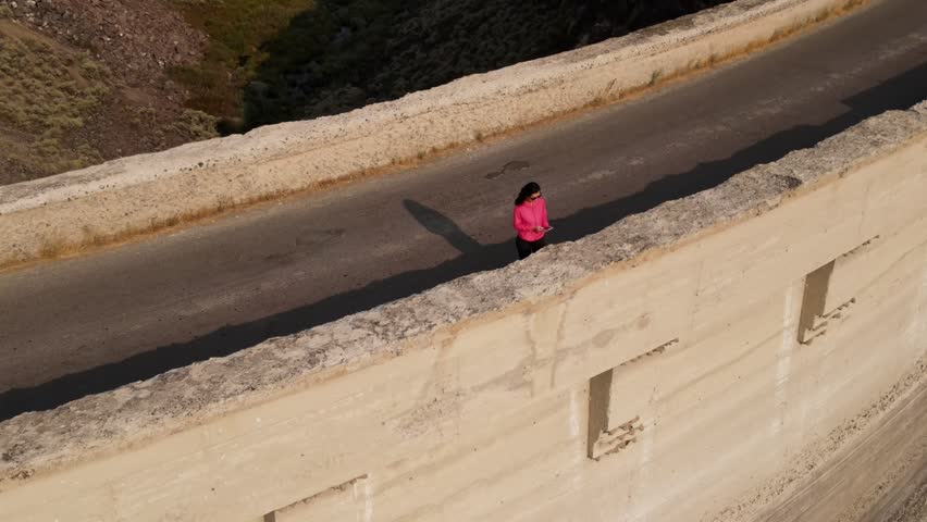 Aerial shot of an Asian woman hiking across the historic 100 year old Salmon Falls Dam in Southern Idaho