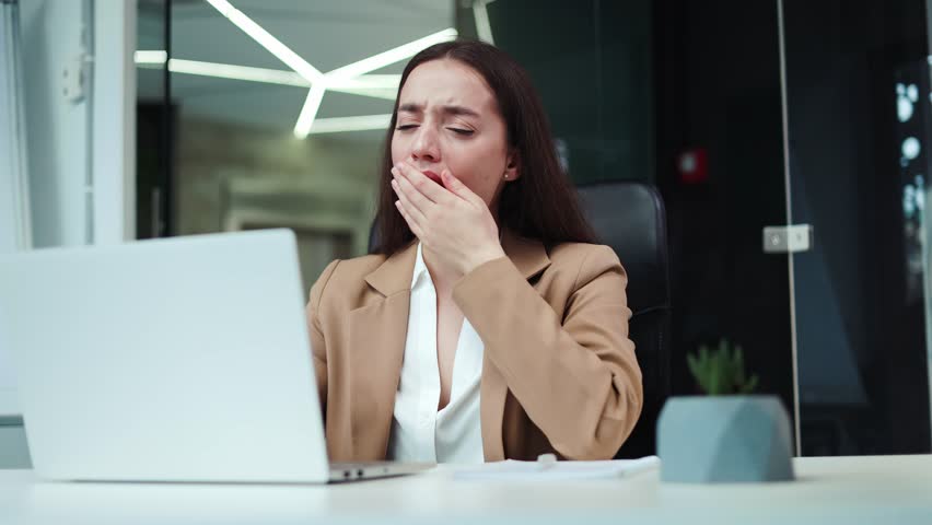 Fatigued woman worker in formal clothes yawning after hard work on portable computer at business center. Exhausted female employee with long brown hair feeling sleepy and needing rest and nap. Royalty-Free Stock Footage #3397105835