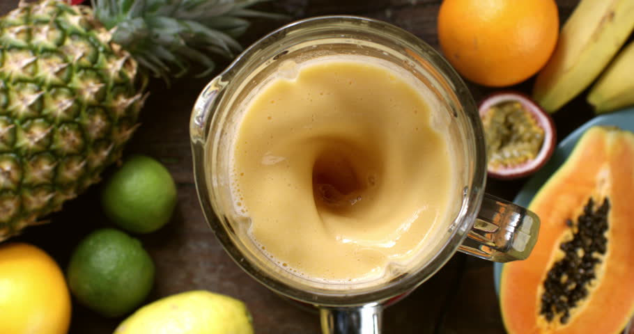 Super slow motion top view of green dietetic milkshake smoothie cocktail of organic fresh exotic and  tropical fruits being mixed in blender at 1000 fps on wooden table of restaurant.