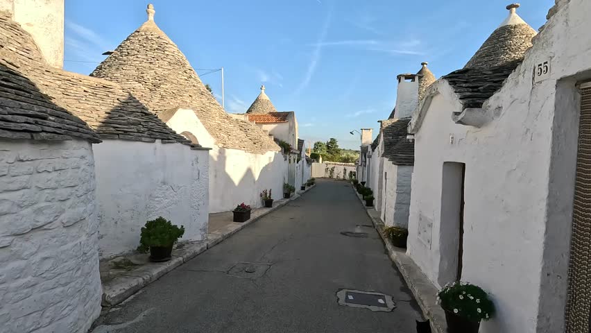Colour Abundance: Alberobello's trulli boast white walls, yet deeper streets reveal a palette of pastel hues on shutters, doors, and flower pots Royalty-Free Stock Footage #3397239457