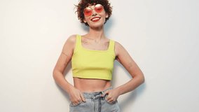 Young beautiful smiling female in trendy summer yellow tank top. Carefree woman posing near white wall in studio with curly hairstyle. Positive model having fun. Cheerful and happy. In sunglasses - Powered by Shutterstock - Get 15% off with code: PIKWIZARD15