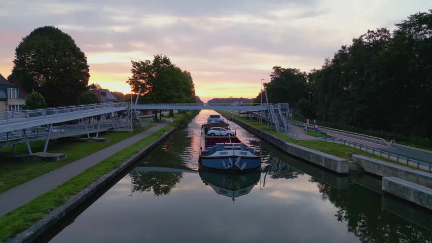 Aerial view of a colourful dramatic sunrise sky over a canal with a cargo boat in Belgium. Canals with water for transport, agriculture. Fields and meadows. Landscape aerial view shot from a drone
