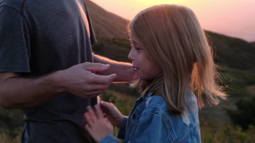 Dad strokes his daughter's head against the backdrop of mountains and the sunset sky. Royalty-Free Stock Footage #3397354449