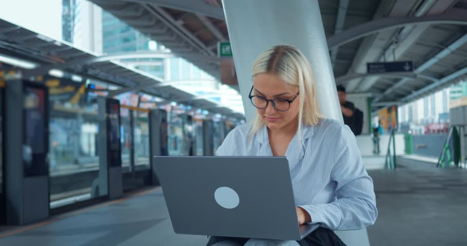 Woman using laptop at subway station metro platform. Modern millennial urban woman sit at subway station, work on laptop remotely. Freelance worker young student work on remote project outside outdoor Royalty-Free Stock Footage #3397376487