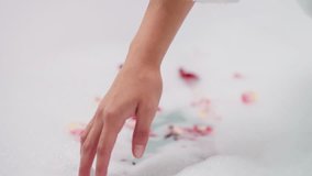 Lady dips hand into foam with rose petals closeup. Woman prepares romantic bath with fresh flowers stirring foam in bathtub. Idea for Valentine day - Powered by Shutterstock - Get 15% off with code: PIKWIZARD15
