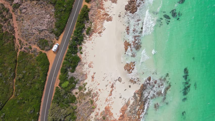 Cinematic top down view of motorhome driving along scenic coastal road in Margaret River, Western Australia at high tide Royalty-Free Stock Footage #3397488315