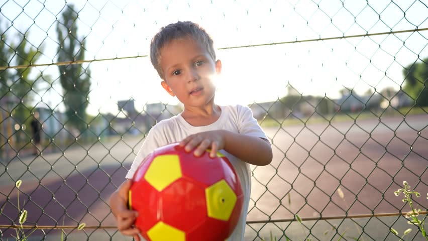 the boy stands near the playground. concept of happy childhood and loving family. child holding a red ball in his hands, playground and glare of the sun in the background lifestyle Royalty-Free Stock Footage #3397533045