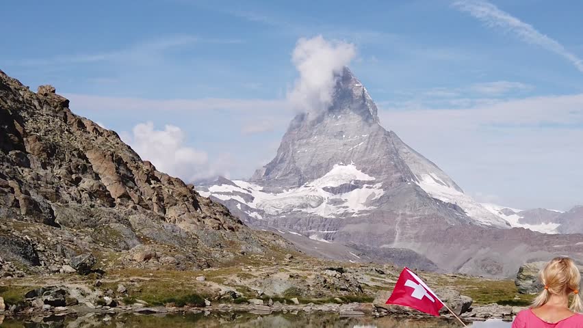 SLOW MOTION: Woman with Swiss flag at Mount Matterhorn or Monte Cervino, reflected on Riffelsee Lake. Tourism in Zermatt,Canton of Valais, Switzerland. Scenic landscape of popular tourist attraction. Royalty-Free Stock Footage #3397537981