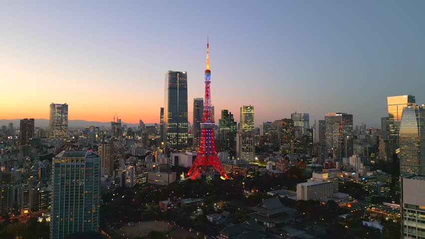 Tokyo, evening, sunset. The camera flies around one of the main symbols of the Japanese capital, Tokyo Tower. High-rise buildings can be seen all around, including the recently opened Azabudai Hiils.