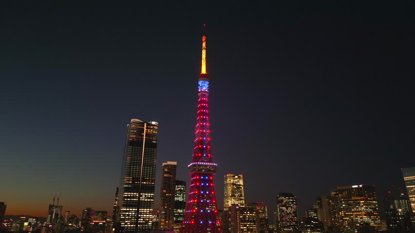 Tokyo, evening, sunset. The camera flies around one of the main symbols of the Japanese capital, Tokyo Tower. High-rise buildings can be seen all around, including the recently opened Azabudai Hiils.