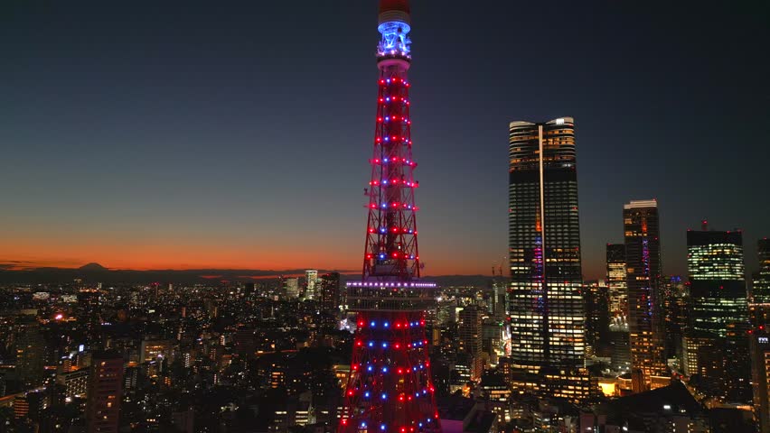 Tokyo, evening, sunset. The camera flies around one of the main symbols of the Japanese capital, Tokyo Tower. High-rise buildings can be seen all around, including the recently opened Azabudai Hiils.