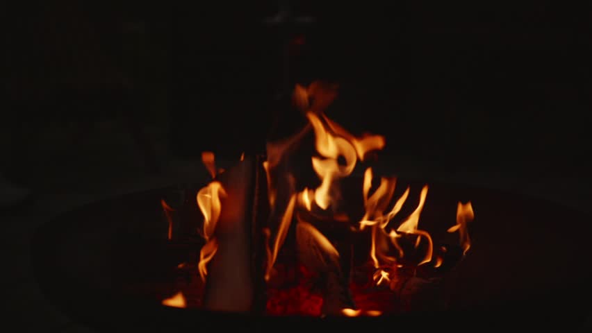 Beautiful cinematic shot in slow motion. A fire is burning in a hearth made of firewood outside in complete darkness. Red coals under the flames. High quality FullHD footage