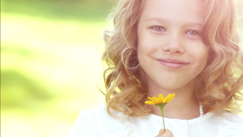 Little girl smelling a daisy flower in the meadow in sunny day. Slow motion