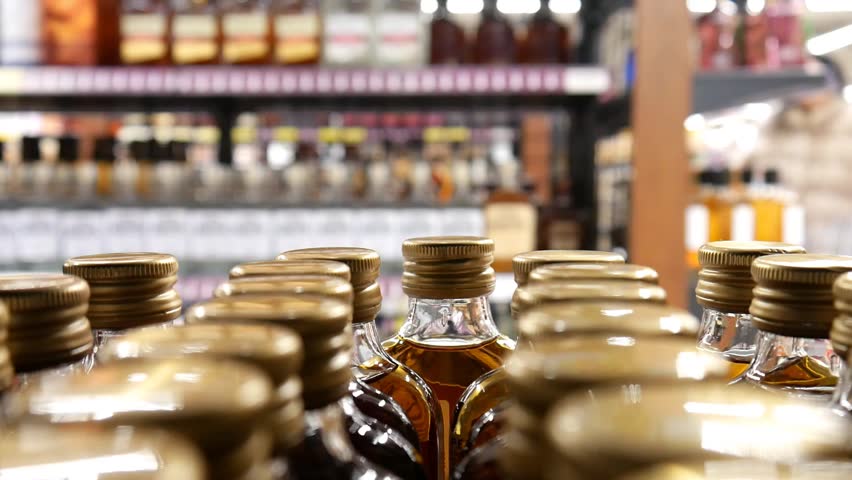 Many bottles of cognac rum or brandy in alcohol department and a male buyer with a shopping trolley takes one