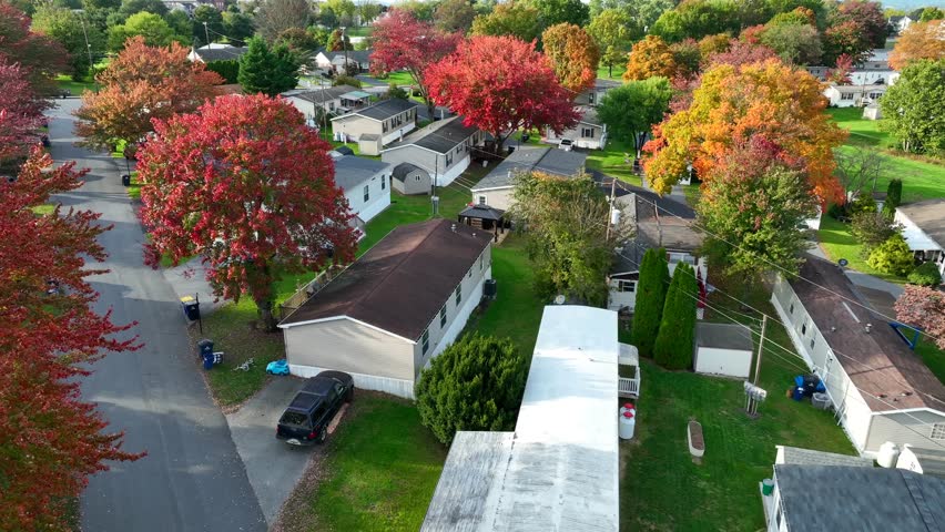 Manufactured homes in American suburb during autumn. Aerial shot of mobile home trailer park with colorful fall trees.