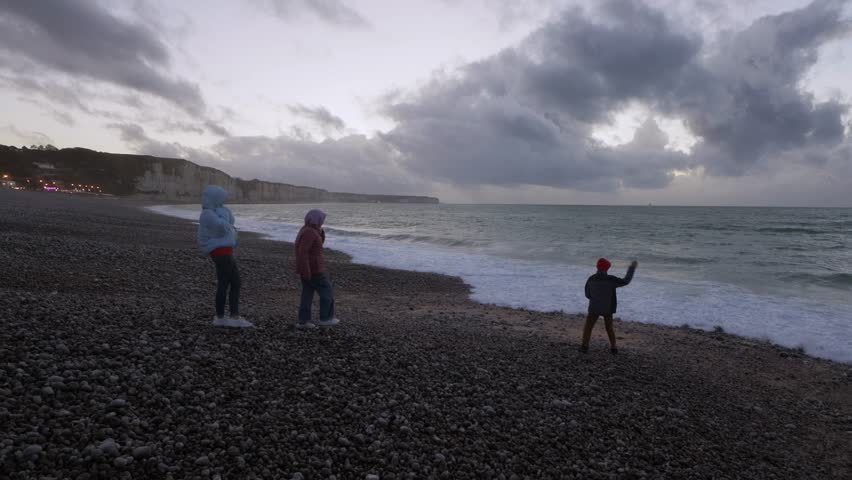 a family stands on the seashore in jackets on a cloudy day, a mother and two children stand