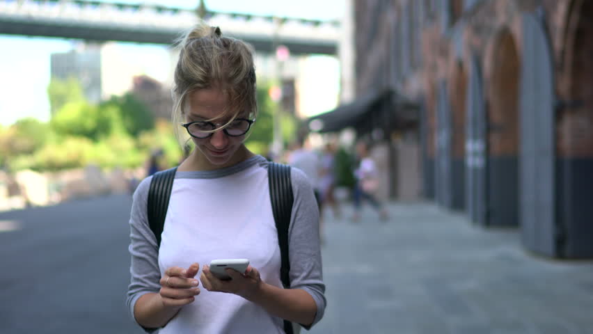  Cheerful female tourist in eyeglasses installing navigator on modern telephone device walking on streets in urban setting.positive traveller strolling and publishing new post on website Royalty-Free Stock Footage #33980566