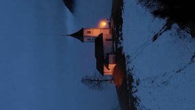 Illuminated Church of St. Primoz and Felicijan at Winter Evening Foggy Twilight. Jamnik, Slovenia. Aerial View. Orbiting. Vertical Video