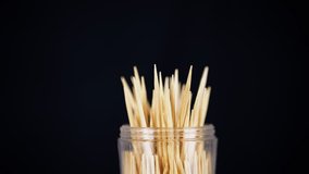 Wooden Toothpicks Rotate on a Black Background. Close up. A set of bamboo toothpicks in a transparent plastic cup. Home oral care after meals. Teeth cleaning. Blurred motion. Dentistry concept. Loop. - Powered by Shutterstock - Get 15% off with code: PIKWIZARD15