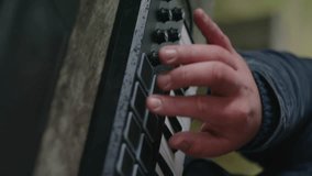Hands close up of Caucasian man pressing buttons and playing on MIDI controller outdoors. Professional male musician uses digital electric piano, creates and records music or new song. Vertical video.