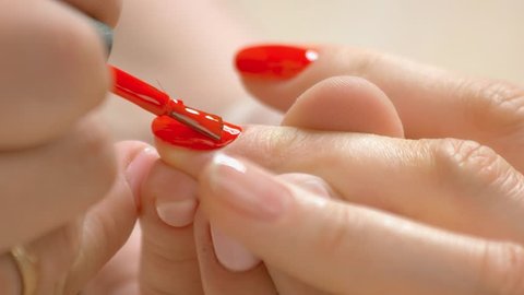 Red varnish applying on nails. Beautiful woman hands receiving manicure by professional manicurist in beauty salon close up. Skin and nails care.