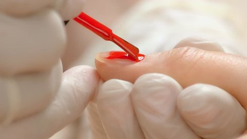 Manicurist accurately applying varnish on nail. Cosmetician in rubber gloves covering female finger nails with red color polish. Women beauty and care.