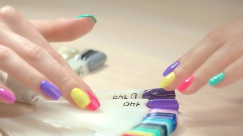 Close up hands and nail polish samples. Girl hand with multicolored summer manicure choosing nail color tester in nail salon. Beautiful hands and collection of nail samples.