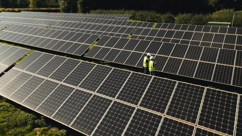 Drone shot of engineers inspecting solar panels in field generating renewable energy - shot in slow motion Adlı Stok Video