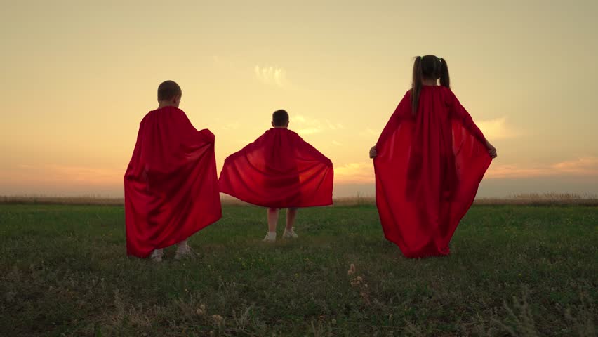 Boy, girl play red cape superhero, childhood dream. Child hero in red cloak running into sunset. Happy children run, play superheroes against sky. Child in raincoat plays. Carnival Children nature. Royalty-Free Stock Footage #3398545285