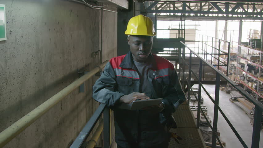 Medium shot of African American male warehouse supervisor in hard hat and overalls typing information on tablet while checking storage items from above Royalty-Free Stock Footage #3398583101