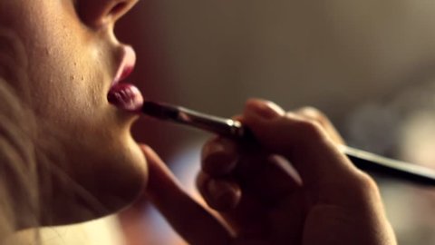 Female make-up artist apply pink lipstick with brush on a client’s lips, close-up.