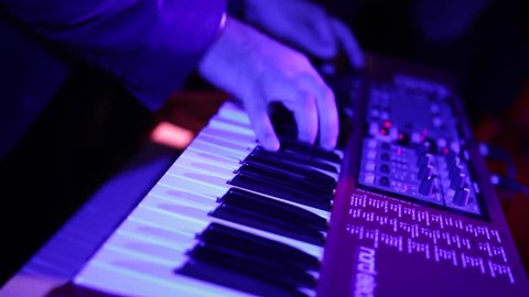 Male hands playing electric piano under colorful stage lighting, close-up. Musician in a suit perform a composition on a keyboard music workstation on a party night. 