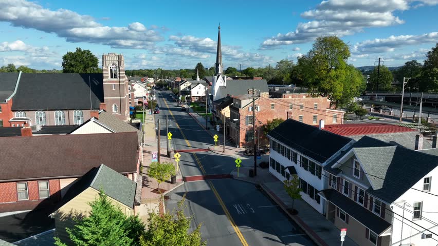 Small town USA during bright autumn day. Aerial shot of houses and churches on main street with American flag.