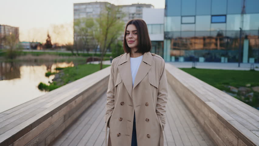 Young Charming Brunette Lady in Trench Standing Outside on the Bridge on the Local Lake. Smiling Cute Girl Outdoors after the University. People Concept Royalty-Free Stock Footage #3398756407
