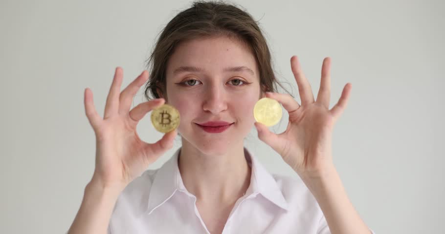 A happy girl brings a close-up to the eyes of bitcoins. Successful trading, cryptocurrency, slowmotion