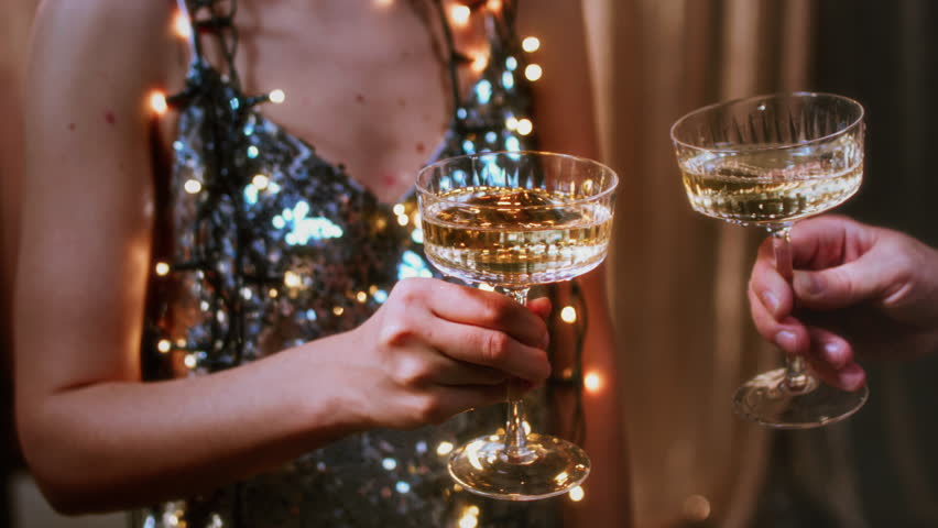 A girl holds glasses of champagne in her hands, cheers with a man. Le coupe cocktail glasses. Celebrates the New Year or a corporate holiday. Disco or retro style. They bump glasses, clink glasses
