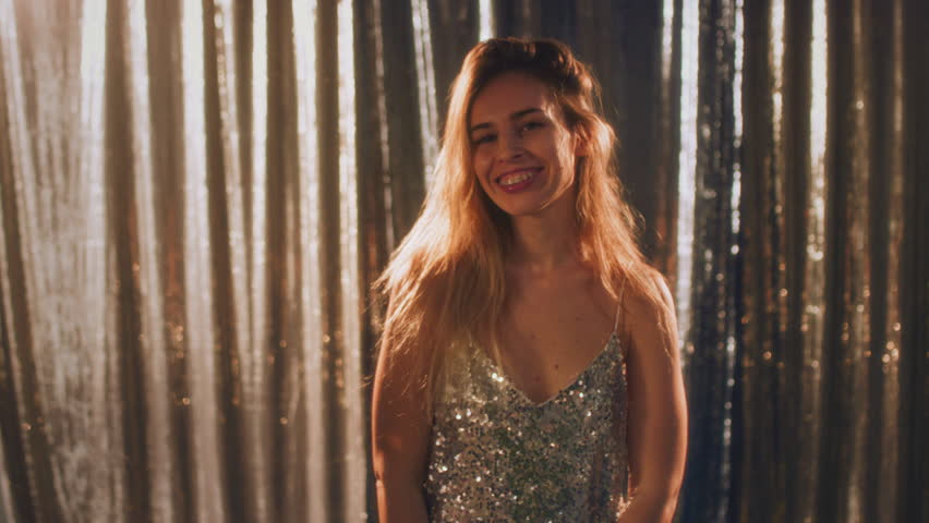 A beautiful girl is dancing on a shiny background. Celebrates the New Year or a corporate holiday. Dancing in a sequined dress. Disco or retro style. Hair moving in slow motion