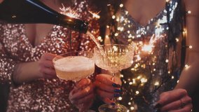 The girls pour champagne into round glasses from a bottle. Women in a sparkling dress. Festive decoration, Christmas garland. Full cocktail creamers - le coupe. The female's hand holds a wine glass - Powered by Shutterstock - Get 15% off with code: PIKWIZARD15