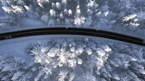 Vertical video. Top view of cars driving through the scenic snowy mountain forest in winter.