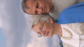 Vertical video. A man of retirement age holds an elderly woman in glasses in his arms.