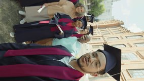 POV shot of student in hat and gown taking selfie with his collegemates and parents during graduation ceremony