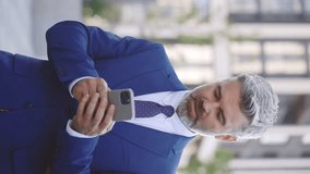 Vertical Video. Handsome Male Boss, Bearded Man, Walking, Using Smartphone, Holding Coffee, and Reading Business News on Smartphone Outdoors. Technology and Communication Concept