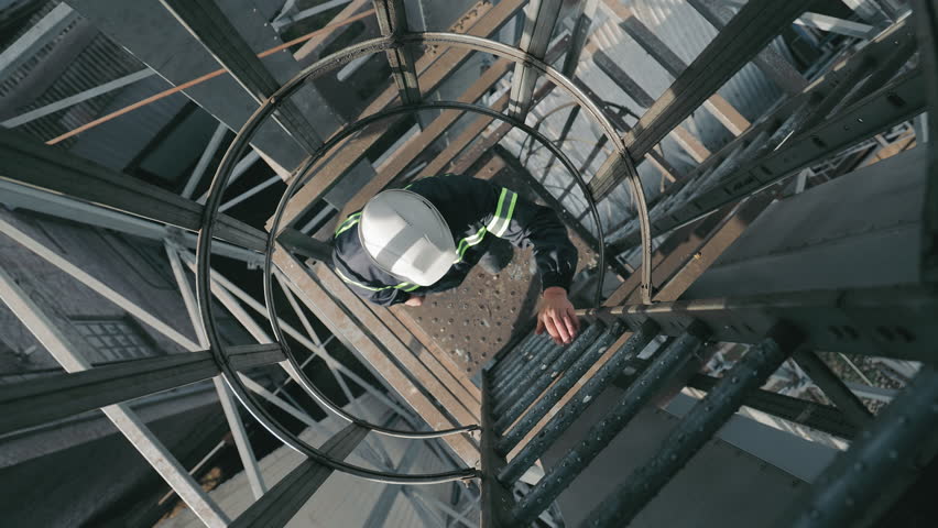 Industrial Worker Climbing Ladders Up. Top view, Worker with hard hat ascending the ladder in an industrial environment.