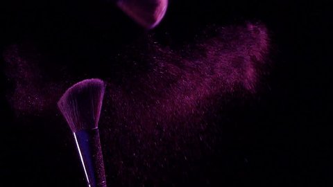 Slow motion of Cosmetic brush with purple cosmetic powder spreading on black background