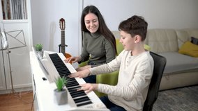 Brother and sister play electric piano at home and have fun. The sister helps her younger brother to play piano