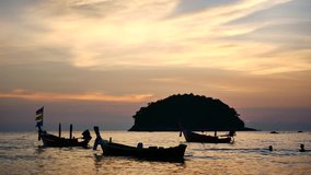 Group of silhouette long tail boat converted to boat excursions floating in the andaman sea with golden light of the Sun before sunset and island background in travel or transportation concept