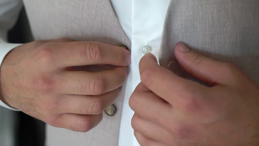 A man is fastening a button on a jacket or vest. Male wears a classic suit. Businessman, office worker or groom. Royalty-Free Stock Footage #3399328457