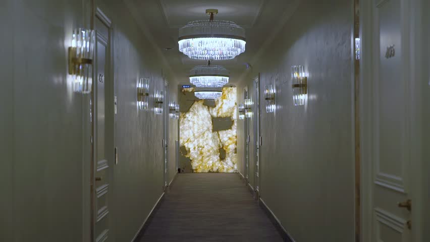 A hallway with lights and a marble wall in hotel. Doors in room numbers or apartments. Luxury residential building indoors.