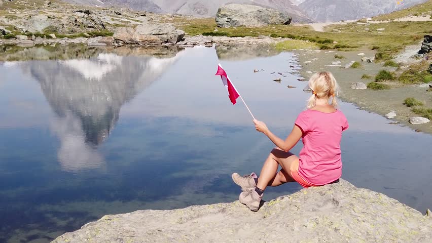 SLOW MOTION: Woman with Swiss flag at Mount Matterhorn or Mont Cervin, reflected on Riffelsee Lake. Tourism in Zermatt,Canton of Valais, Switzerland. Scenic landscape of popular tourist attraction Royalty-Free Stock Footage #3399380529