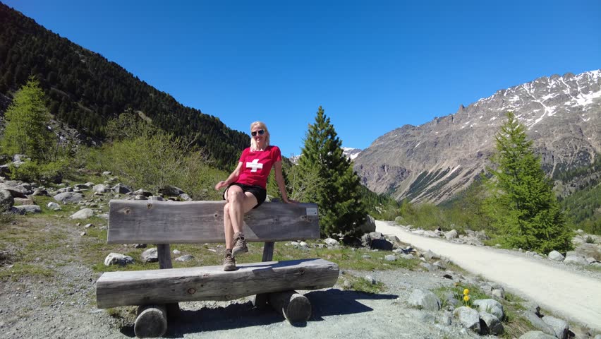 Woman with swiss flag t-shirt on the trekking trail to Morteratsch glacier of Switzerland. Biggest glacier in Bernina Range of the Bundner Alps in Grisons Graubunden Canton of Switzerland.